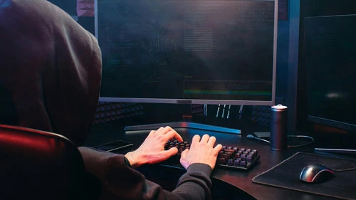 Hooded threat actor typing on a keyboard