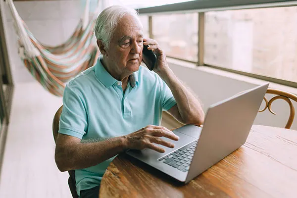 Elderly man with a laptop making a phone call